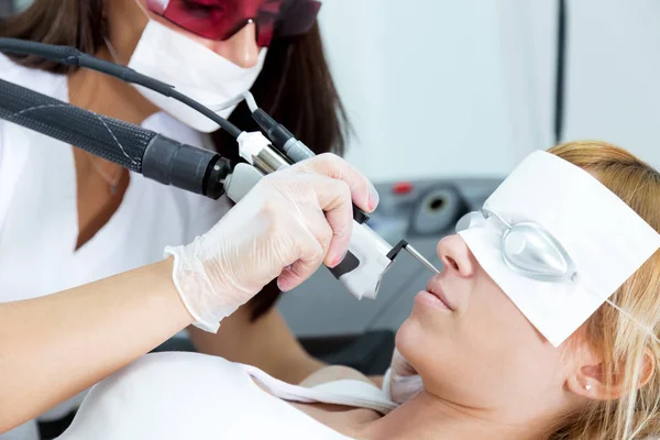 Joven esteticista quitando vello facial con un láser a su cliente en el salón de belleza . — Foto de Stock