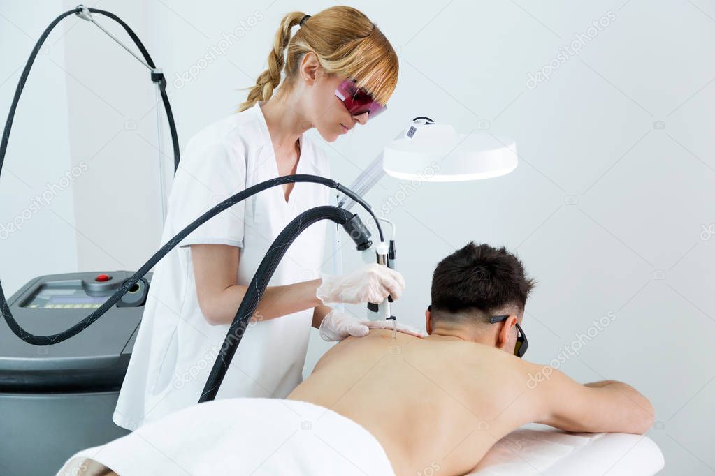 Young beautician removing back hair with a laser to her client in the beauty salon.