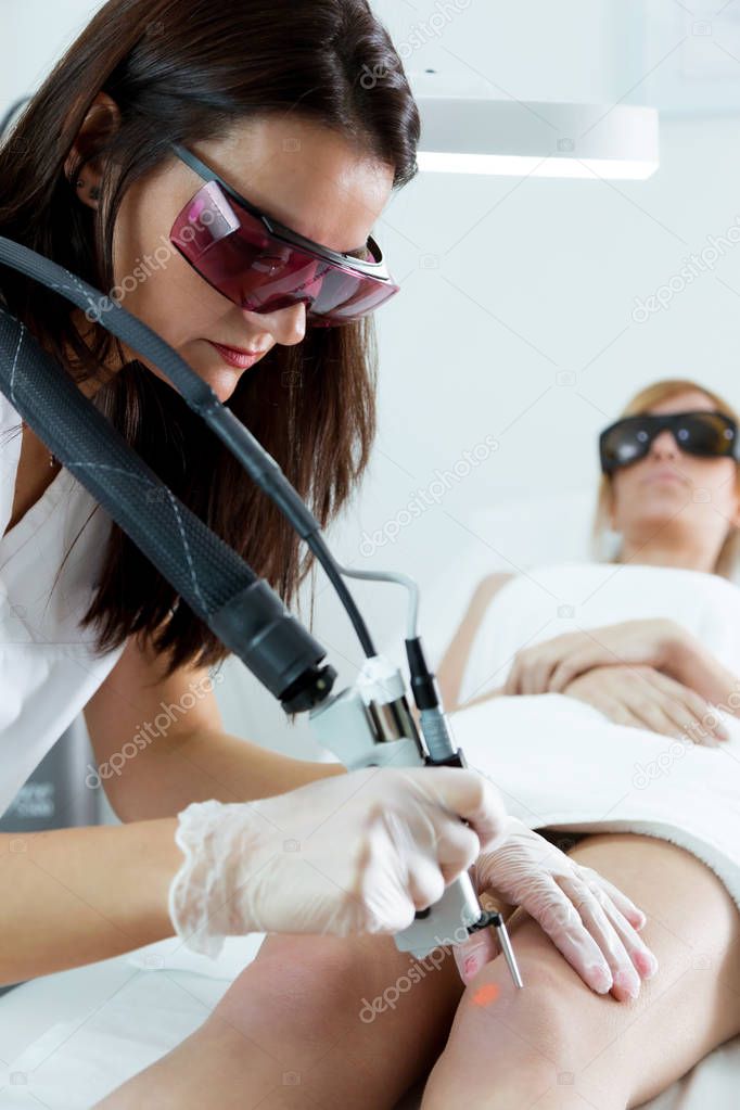 Young beautician removing legs hair with a laser to her client in the beauty salon.