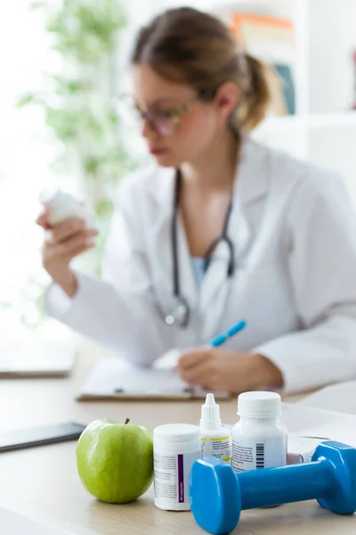 Dietista femminile con un supplemento nutrizionale mentre scrive le proprietà nella consultazione . — Foto Stock