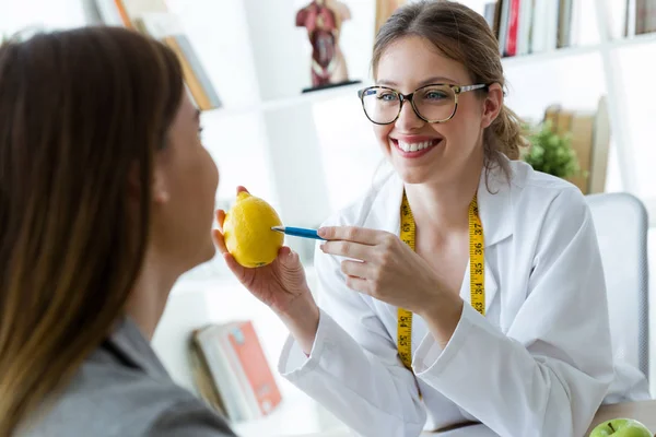 Красивий молодий дієтолог пояснює своїй пацієнтці властивості лимона в консультації . — стокове фото