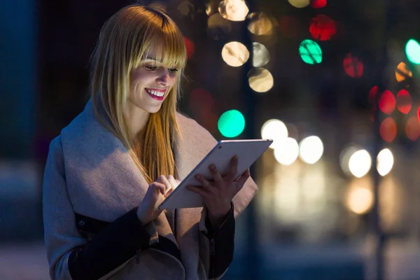 Όμορφη νεαρή γυναίκα με τη χρήση της ψηφιακή ταμπλέτα στο δρόμο τη νύχτα. — Φωτογραφία Αρχείου