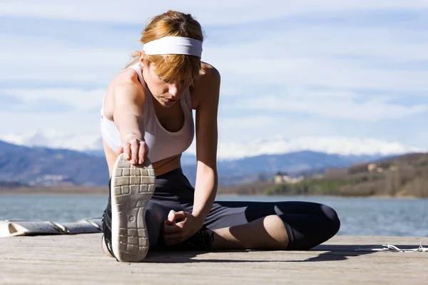 Fitte und sportliche junge Frau beim Stretching am See. — Stockfoto