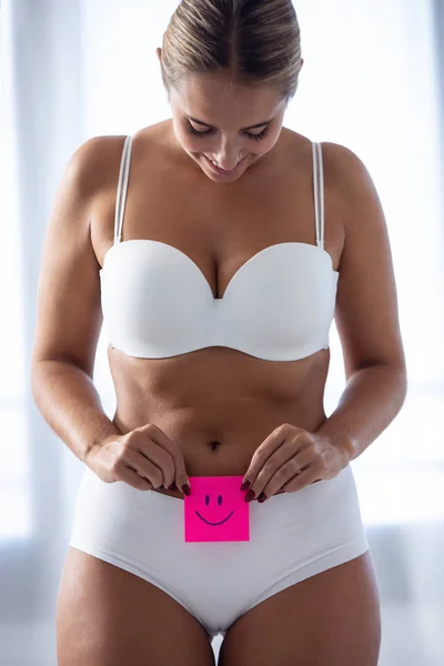 Mujer bastante joven sosteniendo papel con sonrisa marca sobre su estómago en casa . —  Fotos de Stock