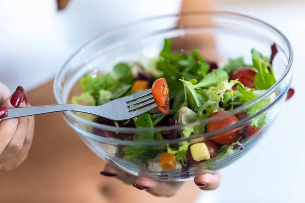 Junge Frau hält Schale mit Salat in der Hand, während sie dies zu Hause isst. — Stockfoto