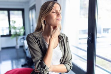 Evdeki oturma odasında dururken boğazı çok kötü ağrıyan genç bir kadın..