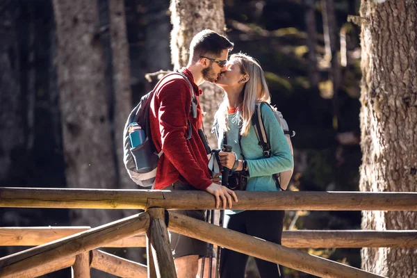 Deux randonneurs avec sac à dos s'embrassant debout sur le pont en bois dans la forêt . — Photo