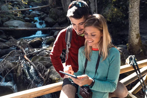 Dois caminhantes de viagem fazendo uma consulta com seu telefone celular na ponte de madeira na floresta . — Fotografia de Stock