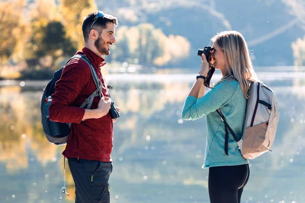 Jovem viajante tirando fotos para o namorado na frente do lago na montanha . — Fotografia de Stock