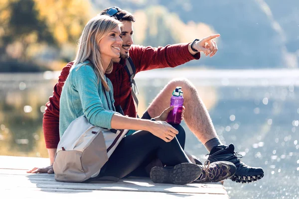 Due escursionisti di viaggio seduti mentre l'uomo indica qualcosa nel paesaggio del lago in montagna . — Foto Stock