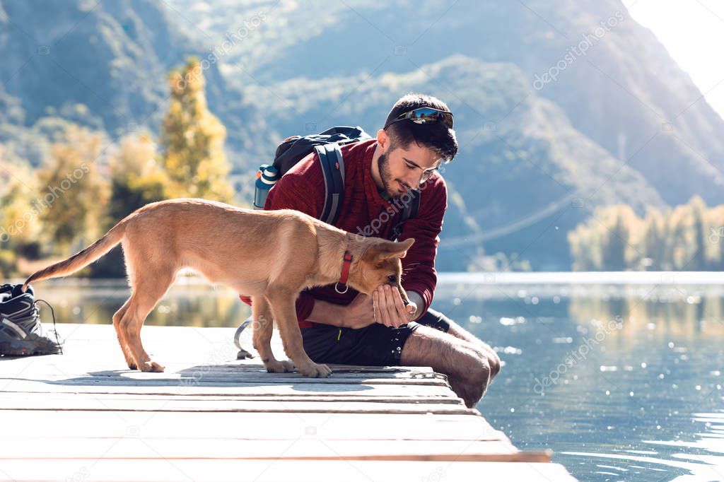 Young traveler hiker with backpack giving water to dog on the lake.