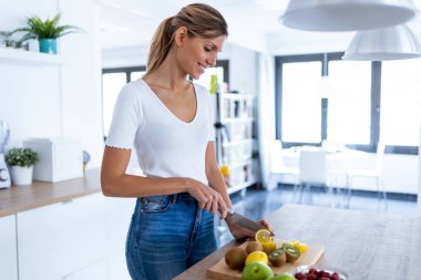 Evdeki mutfakta detoks içeceği hazırlamak için limon kesen genç ve güzel bir kadın..