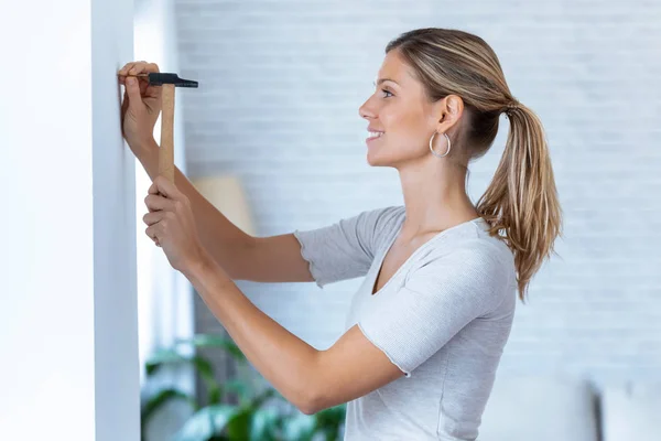 Hübsche junge Frau schlägt zu Hause mit dem Hammer einen Nagel in eine Wand. — Stockfoto