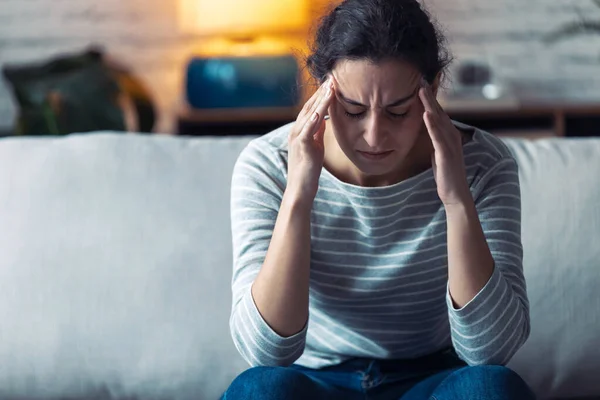 Ung kvinna med huvudvärk sitter på soffan i vardagsrummet hemma. — Stockfoto