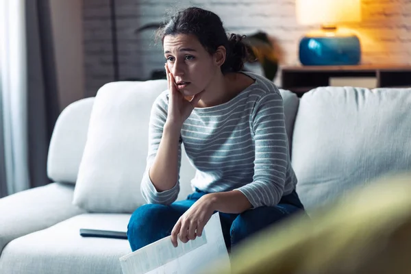 Besorgte junge Frau denkt über ihre Probleme nach, während sie Rechnungen von zu Hause hält. — Stockfoto