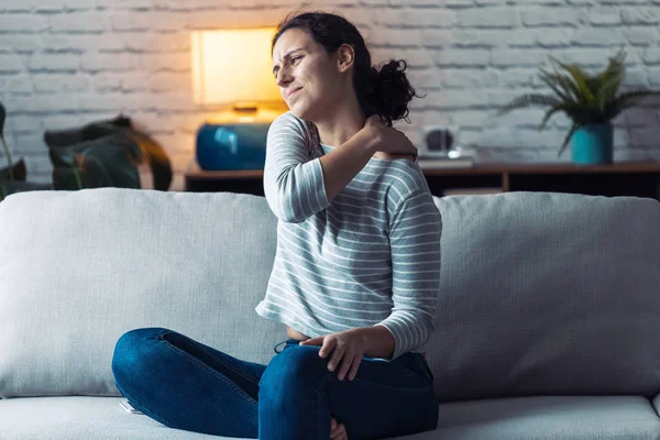 Mujer joven con dolor de espalda sentada en el sofá en la sala de estar en casa . — Foto de Stock