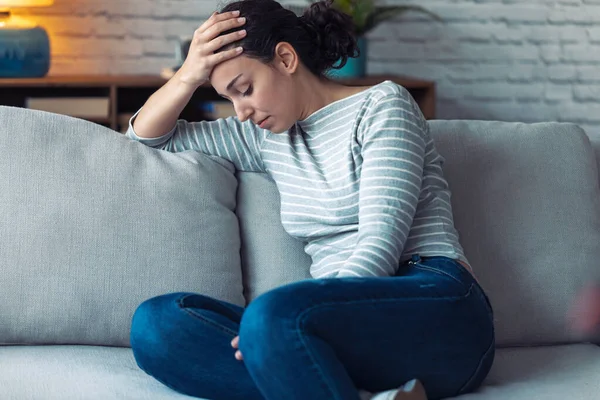 Deprimerad ung kvinna tänker på sina problem när hon sitter på soffan hemma. — Stockfoto