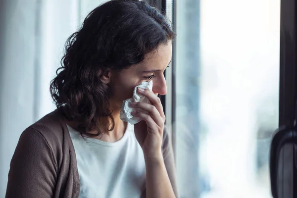 Sad young woman crying while looking through the window at home. — Stock Photo, Image