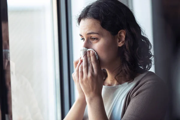Θλιβερή νεαρή γυναίκα κλαίει κοιτάζοντας από το παράθυρο στο σπίτι. — Φωτογραφία Αρχείου