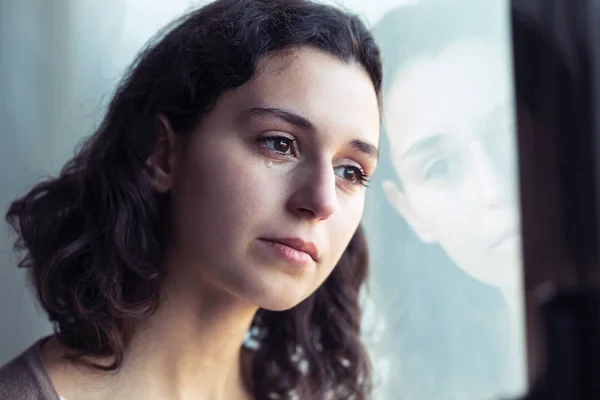 Traurige junge Frau weint beim Blick aus dem Fenster zu Hause. — Stockfoto