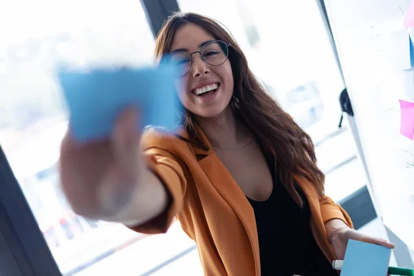 Mujer joven de negocios mirando a la cámara mientras trabaja con pegatinas post it en la oficina . — Foto de Stock