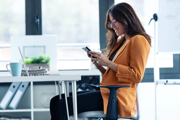 Бізнес молода жінка використовує свій мобільний телефон, сидячи в офісі . — стокове фото