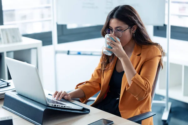 Jovem de negócios bebendo café enquanto trabalhava com laptop no escritório . — Fotografia de Stock