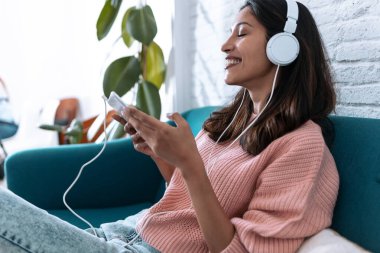 Evdeki kanepede otururken dijital tabletle müzik dinleyen güzel bir genç kadın..