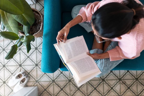 Söt ung kvinna läser en bok när hon sitter på soffan hemma. — Stockfoto