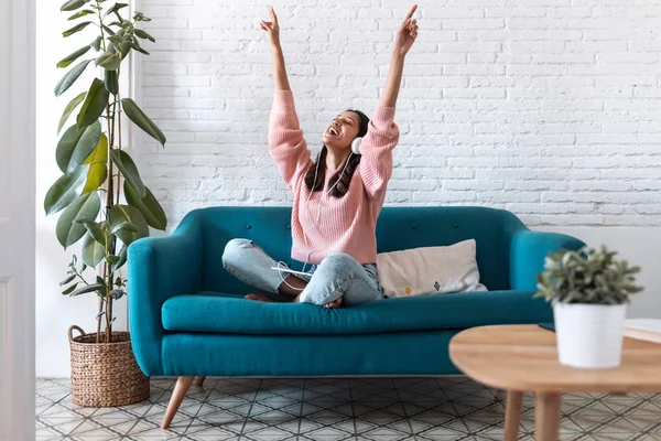 Mujer joven motivada escuchando música con tableta digital mientras está sentada en el sofá en casa . — Foto de Stock