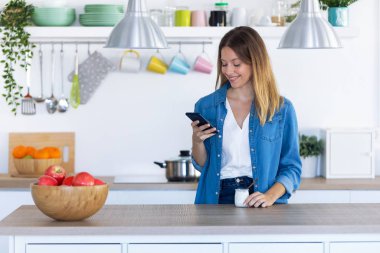Evde mutfakta yoğurt yerken onun cep telefonu kullanarak Pretty genç kadın.