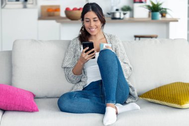 Evde kanepede kahve içerken onun cep telefonu kullanarak Pretty genç kadın.