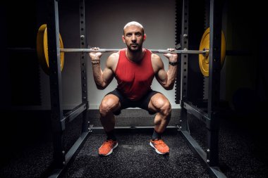 Güçlü kaslı vücut geliştirici atletik adam karanlık stüdyoda halterle kaslarını şişiriyor..