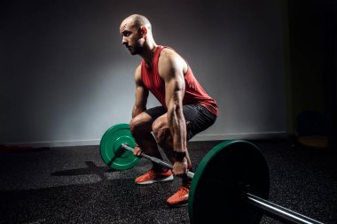 Strong muscular bodybuilder athletic man pumping up muscles with barbell on dark studio. clipart