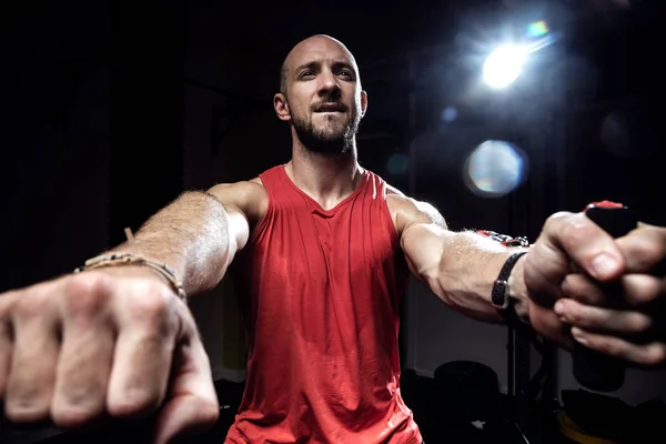 Muskulöser Mann während des Trainings mit Spanngurten am dunklen Studio. — Stockfoto