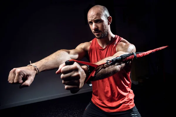 Uomo muscolare durante l'allenamento con cinghie di sospensione TRX in studio scuro . — Foto Stock