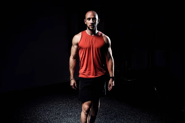 Fuerte musculoso culturista atlético hombre mirando a la cámara mientras está de pie en el estudio oscuro . — Foto de Stock