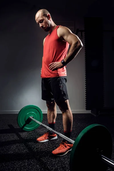 Strong muscular bodybuilder athletic man preparing for training with barbell on dark studio. — Stock Photo, Image