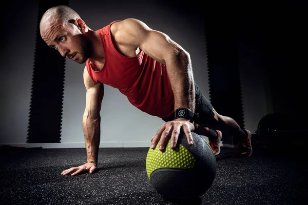 М'язистий молодий чоловік робить підштовхування з медичним м'ячем на темній студії . — стокове фото
