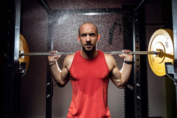 Forte fisiculturista muscular atlético homem bombeando os músculos com barbell no estúdio escuro . — Fotografia de Stock