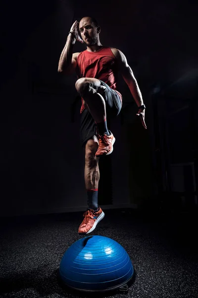 Вмістити спортсмена, що виконує вправи на гімнастичній півкулі босу м'яч на темній студії . — стокове фото
