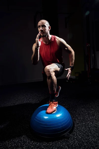 Atleta in forma che esegue esercizio su palla bosu emisfero ginnico su studio scuro . — Foto Stock