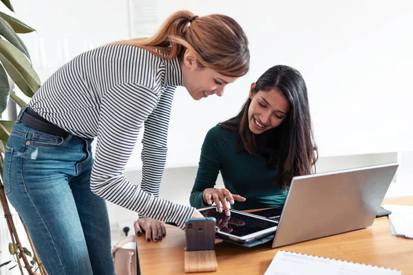 Deux jeunes femmes d'affaires parlent et passent en revue leur dernier travail sur la tablette numérique au bureau . — Photo