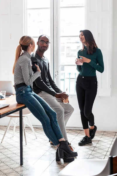 Three young business people drinking coffee while taking a break in the office.