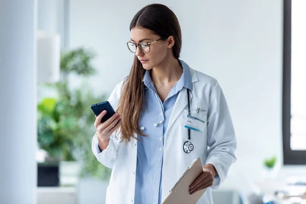 Bella medico femminile utilizzando il suo telefono cellulare mentre in piedi in consultazione medica . — Foto Stock