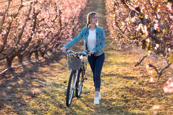 Bella giovane donna che cammina con una bicicletta nel campo di ciliegie in primavera . — Foto Stock