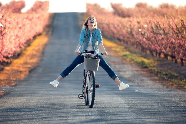 Гарненька молода жінка з вінтажним велосипедом насолоджується часом у вишневому полі навесні . — стокове фото