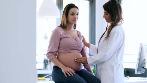 Όμορφη νεαρή γυναίκα γυναικολόγος ελέγχει την καρδιά του μωρού της εγκύου ασθενούς στην κλινική. — Αρχείο Βίντεο