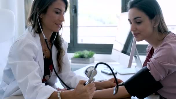Ładna młoda kobieta ginekolog sprawdzanie ciśnienia krwi jej ciężarnej pacjentki w klinice. — Wideo stockowe