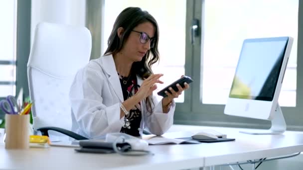 Hübsche junge Gynäkologin mit ihrem Handy vor Beginn der Sprechstunde in der Klinik. — Stockvideo